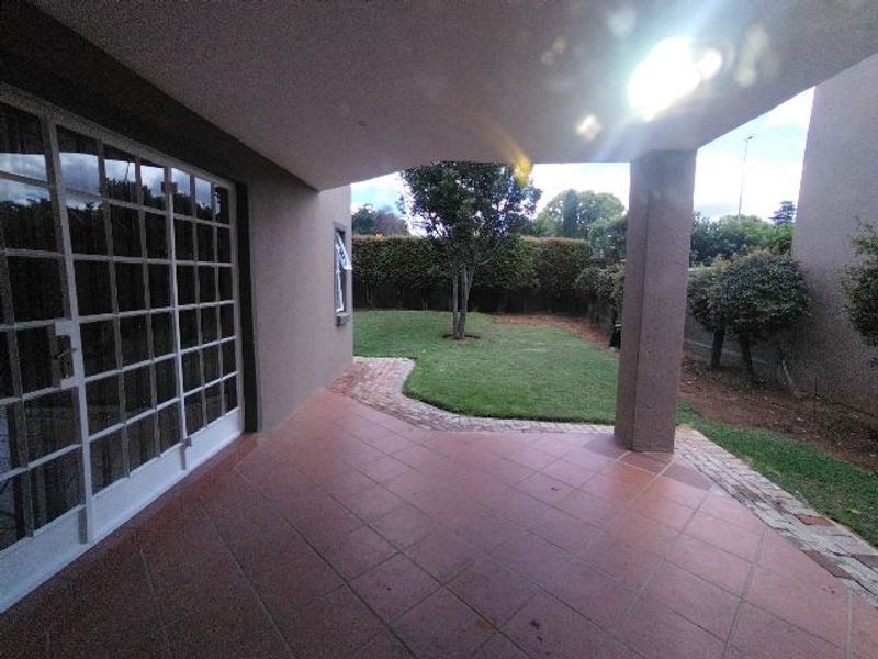 A covered patio area with tiled flooring, featuring direct access to the rear garden through large sliding glass doors.