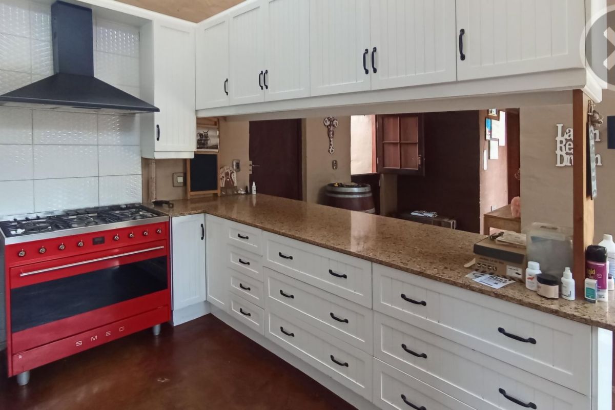 A functional kitchen featuring white cabinetry, granite countertops, and a prominent red gas stove with an integrated extractor fan.