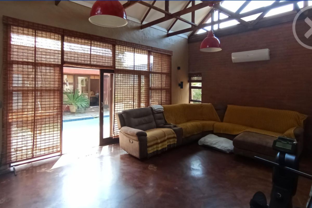 Spacious living room featuring exposed brick walls, polished concrete floors, and high vaulted ceilings with timber trusses, opening directly to the pool area.