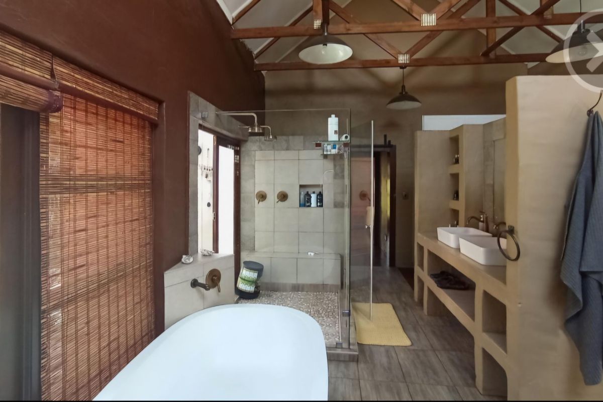 Spacious bathroom featuring exposed timber roof trusses, a freestanding bathtub, a walk-in shower, and a double vanity with built-in storage.