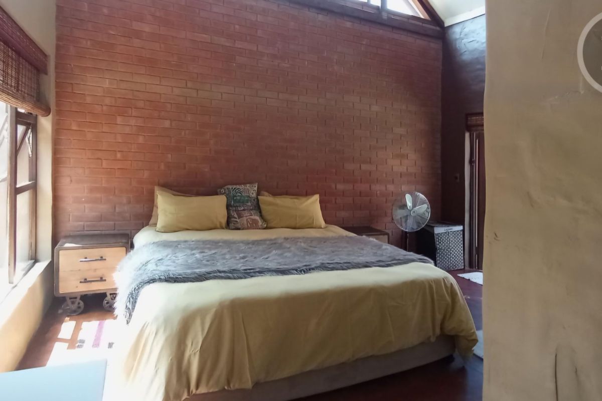A bedroom featuring an exposed brick feature wall, timber flooring, and a vaulted ceiling with large windows providing natural light.