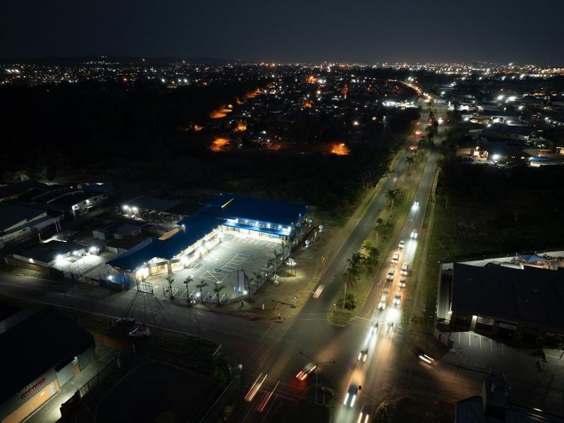 Nighttime aerial view of a commercial property featuring a paved parking area, secure perimeter fencing, and exterior lighting situated along a main road.