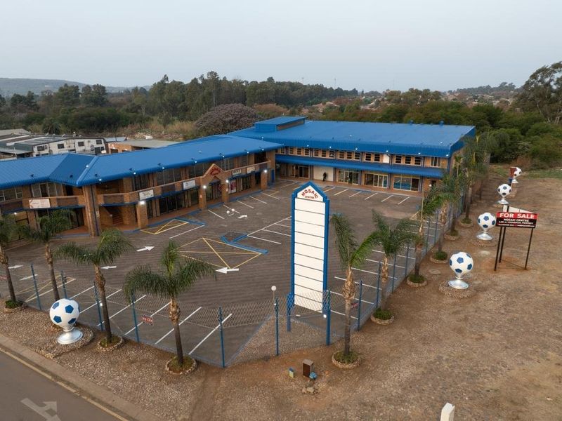 Aerial view of a commercial property featuring a blue metal roof, paved parking lot, and prominent signage pylon.