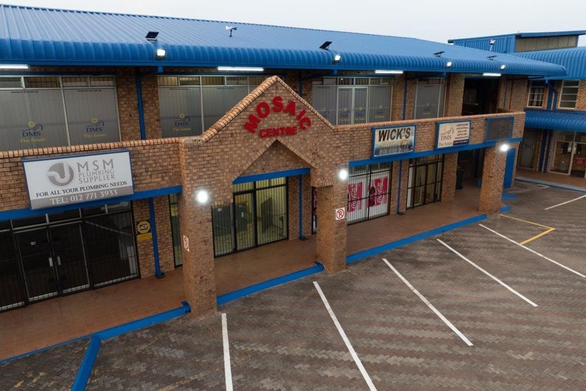 Aerial view of the Mosaic Centre, a commercial property featuring a brick facade, metal roofing, and a paved parking area with multiple storefronts.