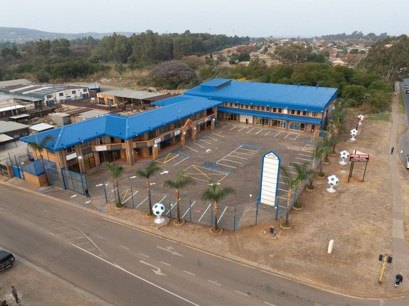 Aerial view of a commercial property featuring a large paved parking lot, blue metal roofing, and perimeter fencing with prominent signage.