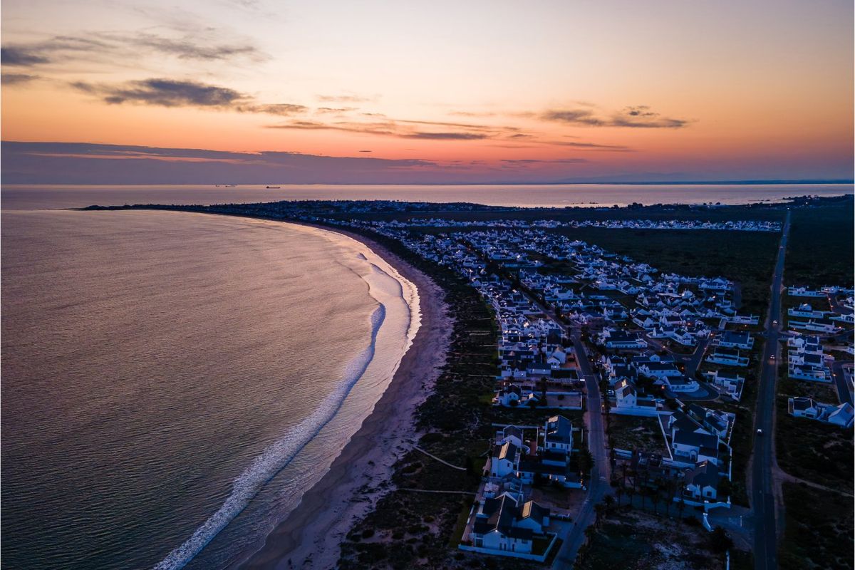 An aerial view of a coastal residential neighborhood at sunset, showcasing the proximity to the beach and the surrounding landscape.