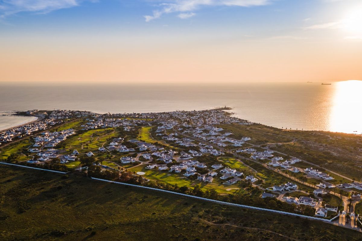 An expansive aerial view of a coastal residential estate featuring a golf course, surrounded by ocean views at sunset.