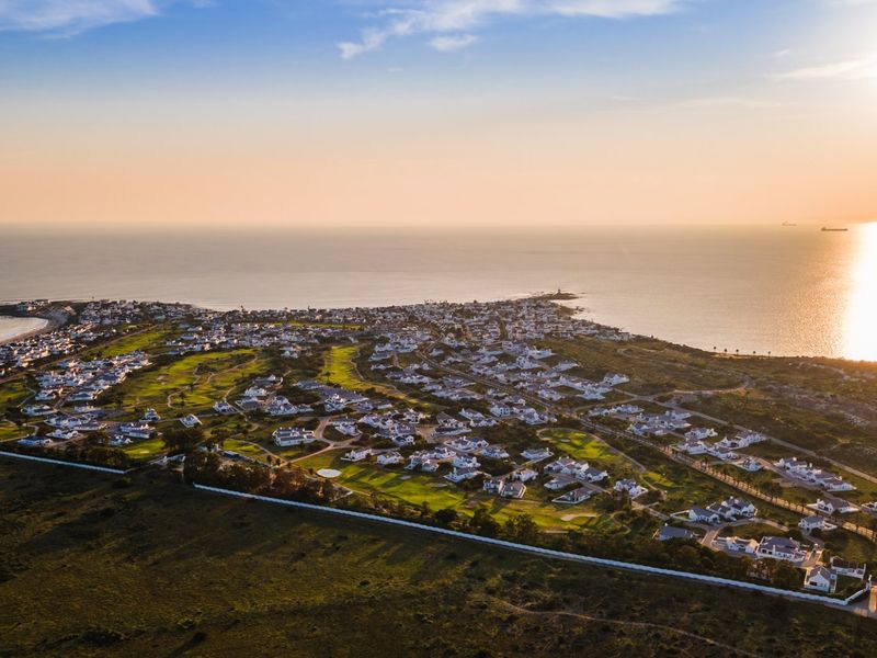 An expansive aerial view of a coastal residential estate featuring a golf course, surrounded by ocean views at sunset.