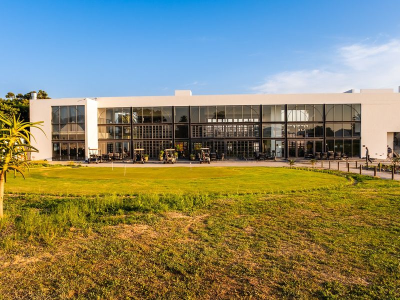 A modern building exterior featuring a large glass facade overlooking a well-maintained lawn and paved patio area.