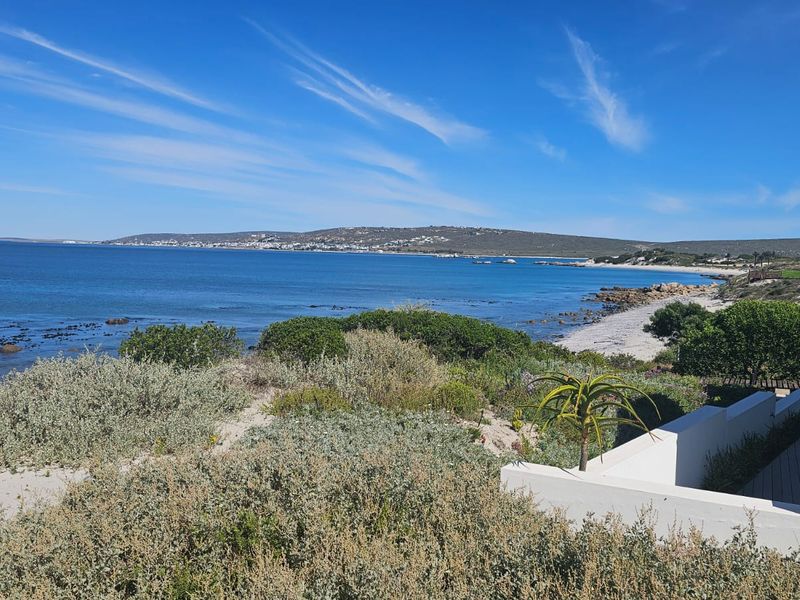 A scenic view of the coastline featuring natural vegetation, sandy terrain, and clear blue ocean waters.