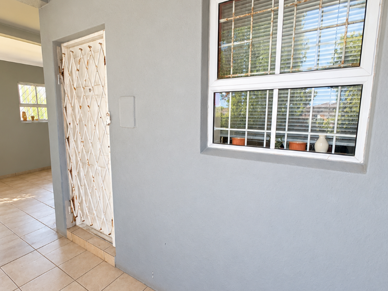 A covered patio area featuring tiled flooring, a security gate, and a window with integrated security bars.