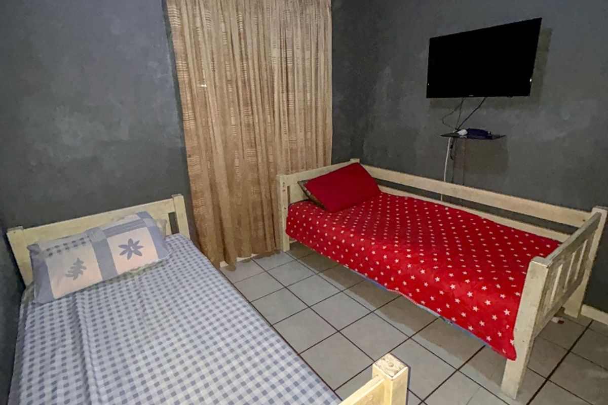 A bedroom featuring tiled flooring and dark grey walls, currently furnished with two single beds.