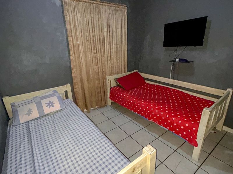 A bedroom featuring tiled flooring and dark grey walls, currently furnished with two single beds.