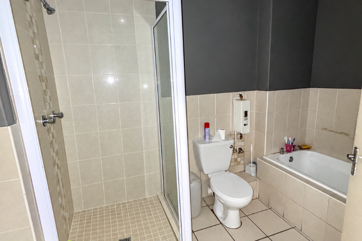 A functional bathroom featuring a separate shower enclosure, bathtub, toilet, and tiled finishes, offering a practical layout for daily use.