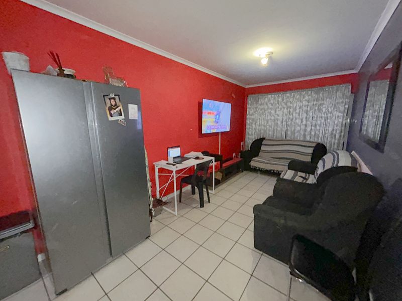 A living room featuring tiled flooring and a coved ceiling, currently utilized as a multi-purpose living and workspace area.