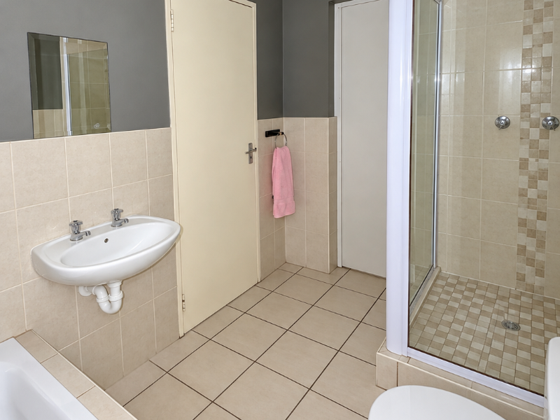 A clean, functional bathroom featuring a separate shower enclosure, bathtub, wall-mounted basin, and toilet with neutral tiled finishes.