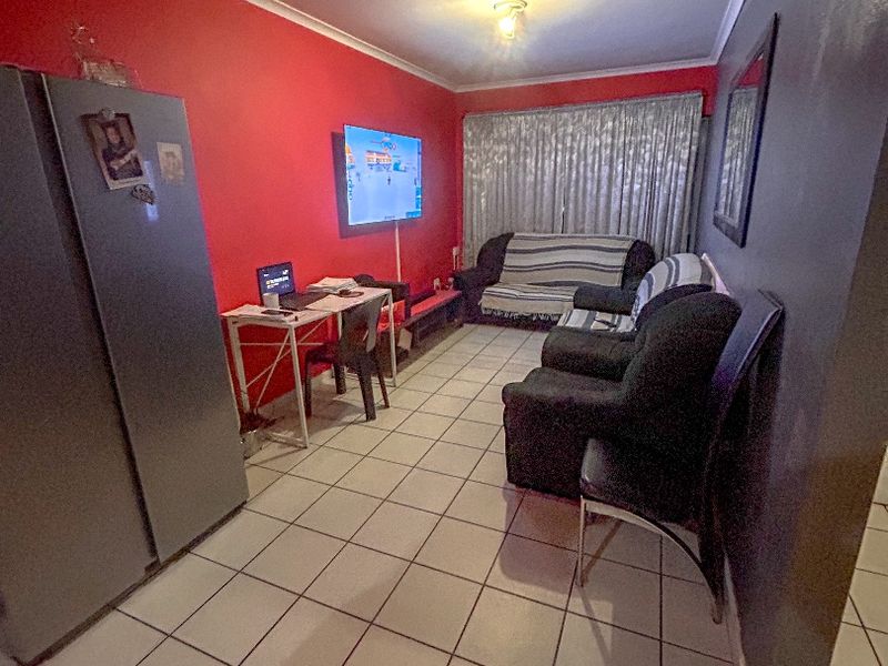 A living room featuring ceramic floor tiles and cove cornice, currently utilized as a multi-functional space.