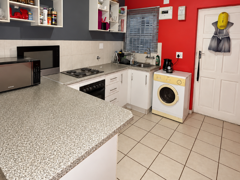 Functional kitchen featuring built-in cabinetry, laminate countertops, an electric hob, oven, and integrated laundry plumbing, finished with tiled flooring and a bold accent wall.
