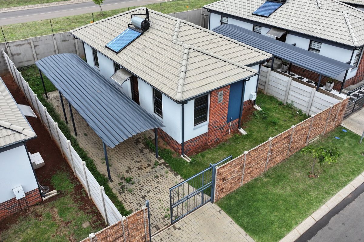 Aerial view of a residential property featuring a tiled roof with solar water heating, a paved carport, and secure perimeter walling.