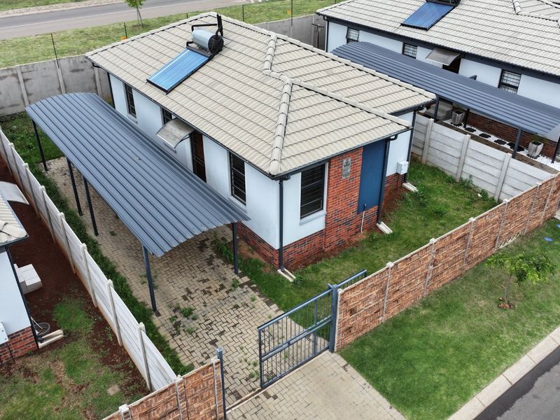 Aerial view of a residential property featuring a tiled roof with solar water heating, a paved carport, and secure perimeter walling.