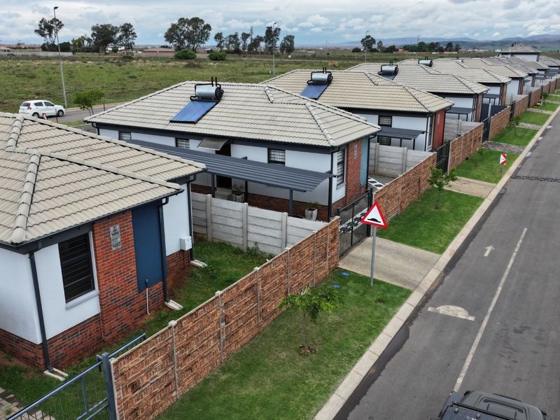 Aerial view of a residential street featuring a row of modern detached houses with tiled roofs, solar water heaters, and private boundary walls.
