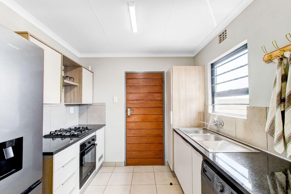 Modern kitchen featuring stone countertops, built-in gas hob, oven, and double sink with ample cabinetry and tiled flooring.