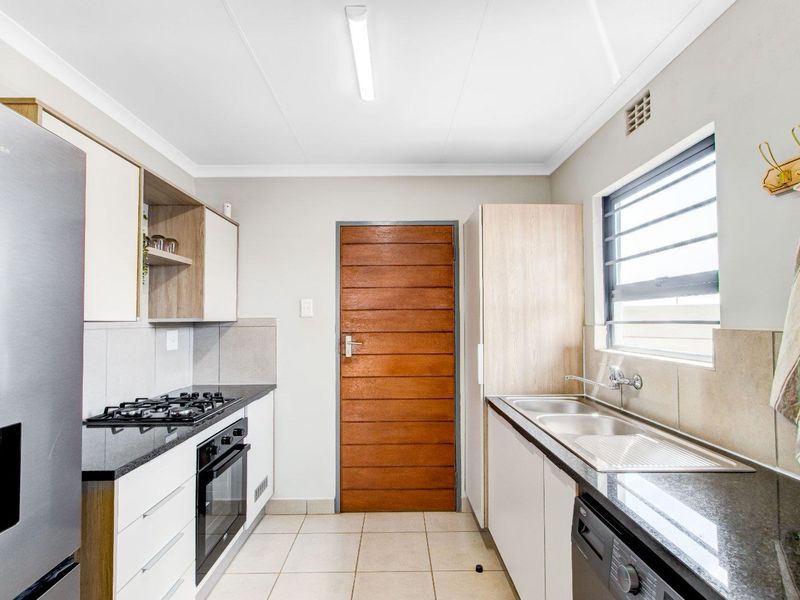 Modern kitchen featuring stone countertops, built-in gas hob, oven, and double sink with ample cabinetry and tiled flooring.