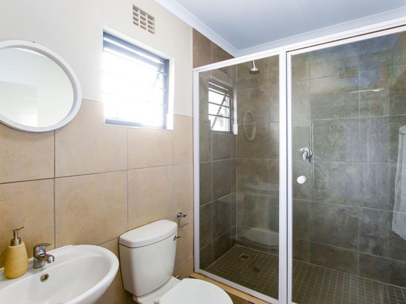 A functional bathroom featuring a glass-enclosed shower, wall-mounted basin, and toilet with neutral-toned wall and floor tiling.