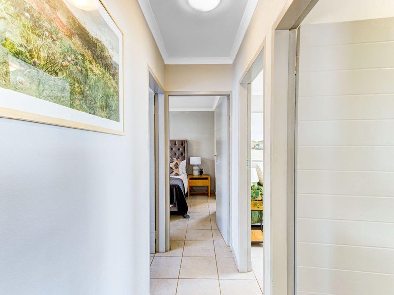 A bright, tiled hallway providing access to adjacent bedrooms, featuring neutral wall tones and clean architectural lines.