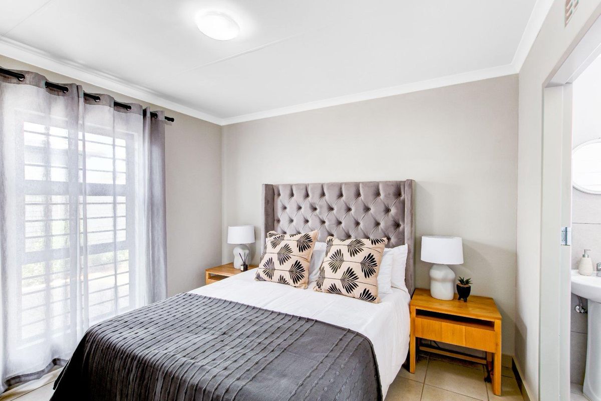A well-maintained bedroom featuring tiled flooring, a sliding glass door for natural light, and direct access to an en-suite bathroom.