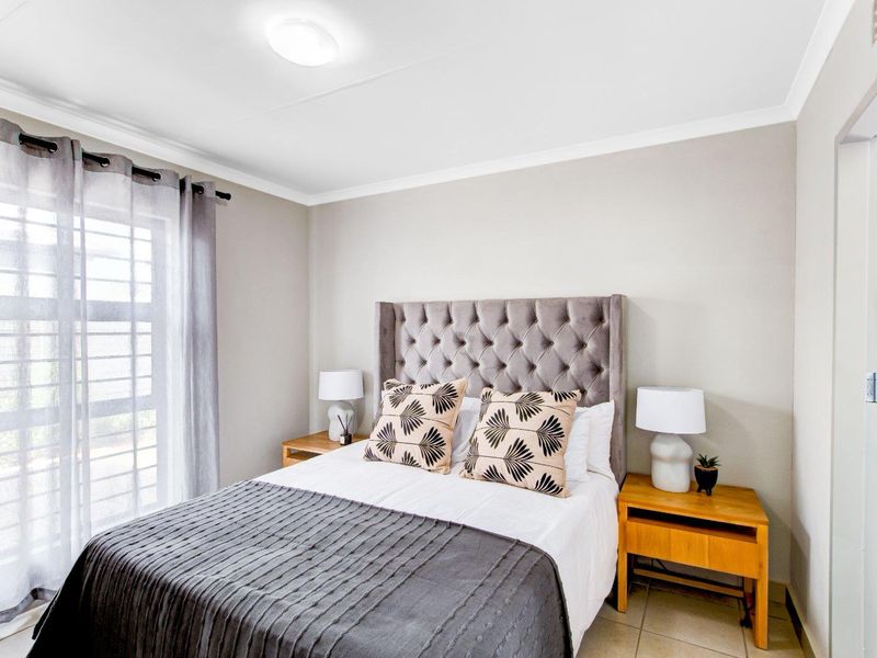 A well-maintained bedroom featuring tiled flooring, a sliding glass door for natural light, and direct access to an en-suite bathroom.