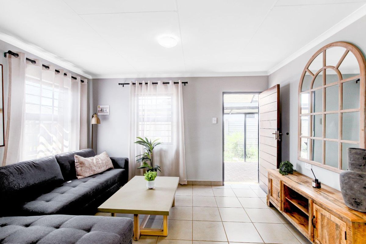 A bright living room featuring tiled flooring, coved ceilings, and direct access to an outdoor patio area through a timber entrance door.