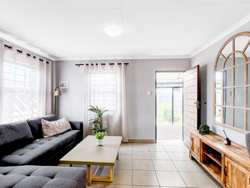 A bright living room featuring tiled flooring, coved ceilings, and direct access to an outdoor patio area through a timber entrance door.