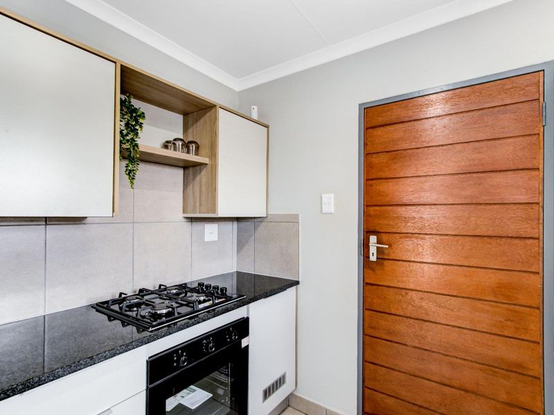 A modern kitchen area featuring built-in cabinetry, granite countertops, a gas hob, and a built-in oven with a wooden door entrance.