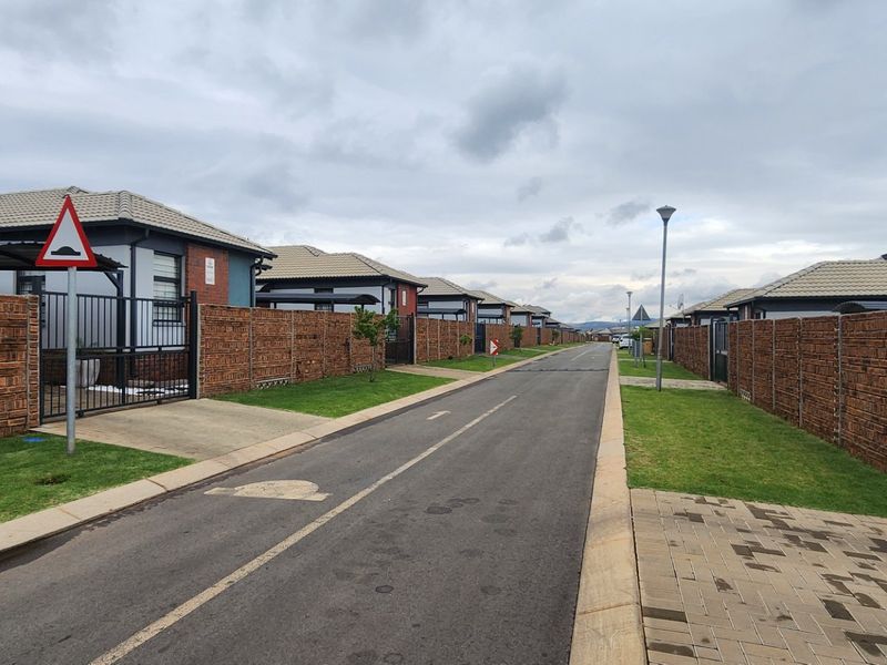 A view of a residential street in a modern estate featuring uniform brick boundary walls, paved driveways, and well-maintained asphalt roads.