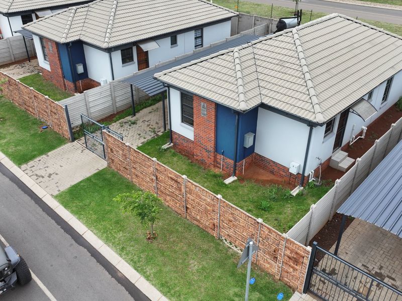 Aerial view of a residential property featuring a tiled roof house, paved driveway, carport, and secure boundary walling in a suburban setting.