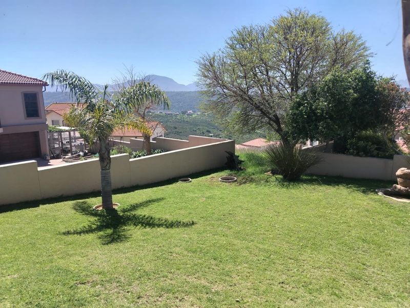 A well-maintained garden area featuring a lawn, retaining wall, and scenic mountain views in the background.
