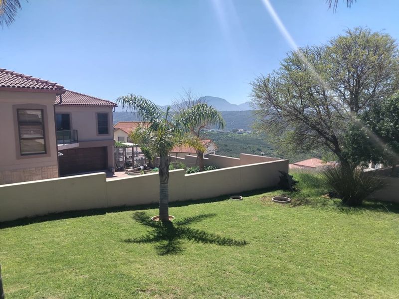 A well-maintained garden area featuring a boundary wall, lawn, and scenic mountain views, adjacent to the property's exterior facade.