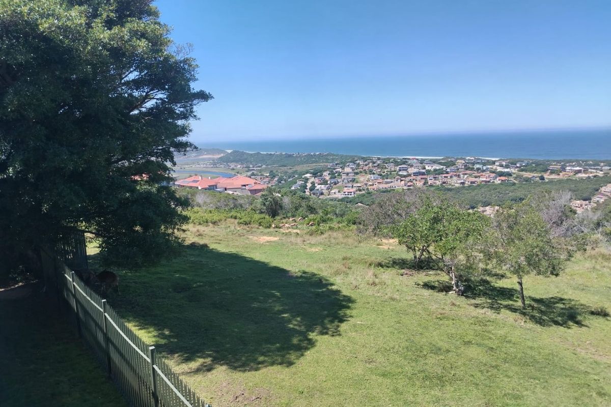 Elevated coastal view overlooking the surrounding residential estate, coastline, and ocean, featuring a grassy foreground and perimeter fencing.
