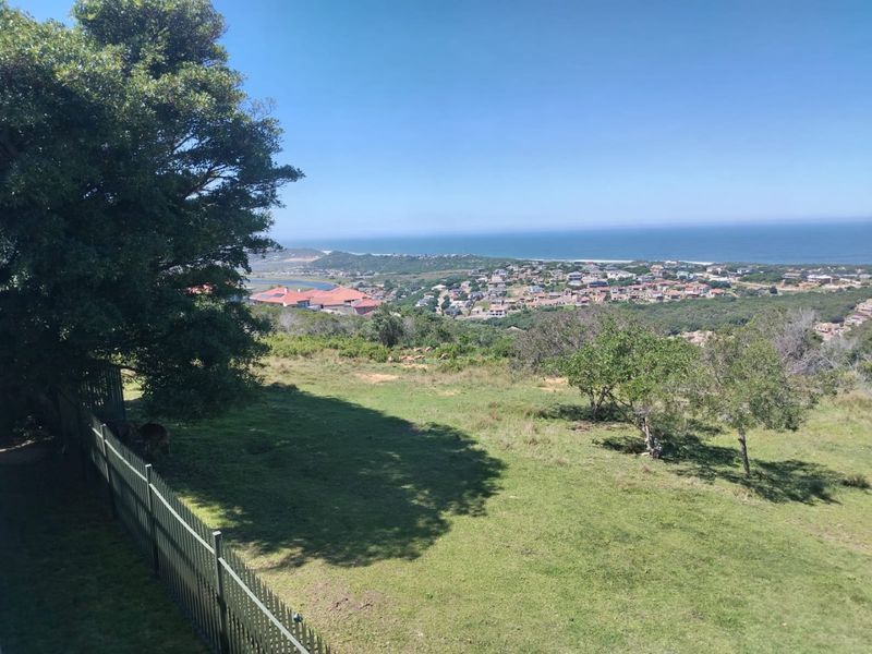 Elevated coastal view overlooking the surrounding residential estate, coastline, and ocean, featuring a grassy foreground and perimeter fencing.