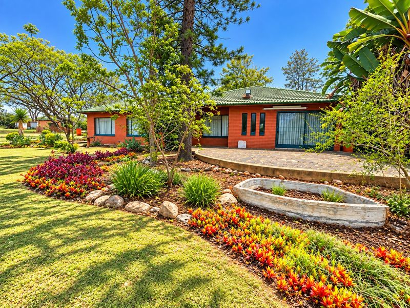 A well-maintained rear exterior view of a brick house featuring a stone-paved patio and a beautifully landscaped garden with vibrant plantings.