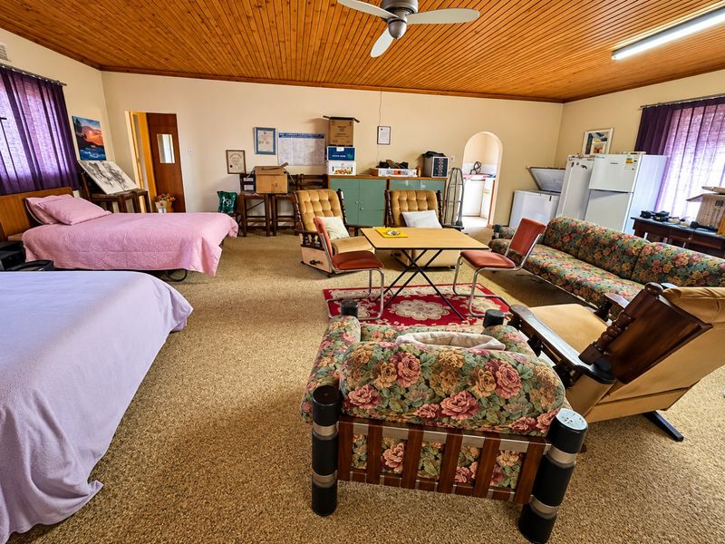 Spacious open-plan living area featuring a timber-clad ceiling, ceiling fan, and carpeted flooring, with an adjacent archway leading to a secondary utility space.