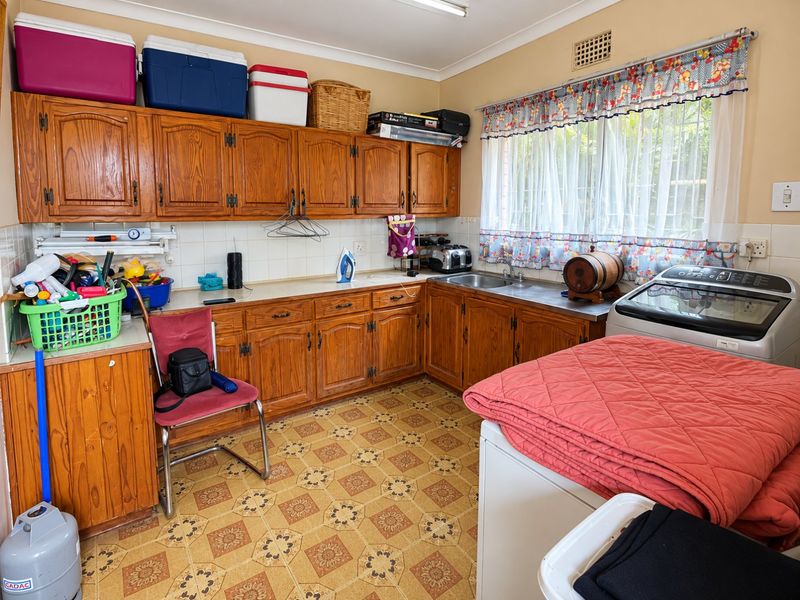 A functional laundry room featuring extensive built-in wooden cabinetry, a stainless steel sink, and durable vinyl flooring, offering ample storage and workspace.