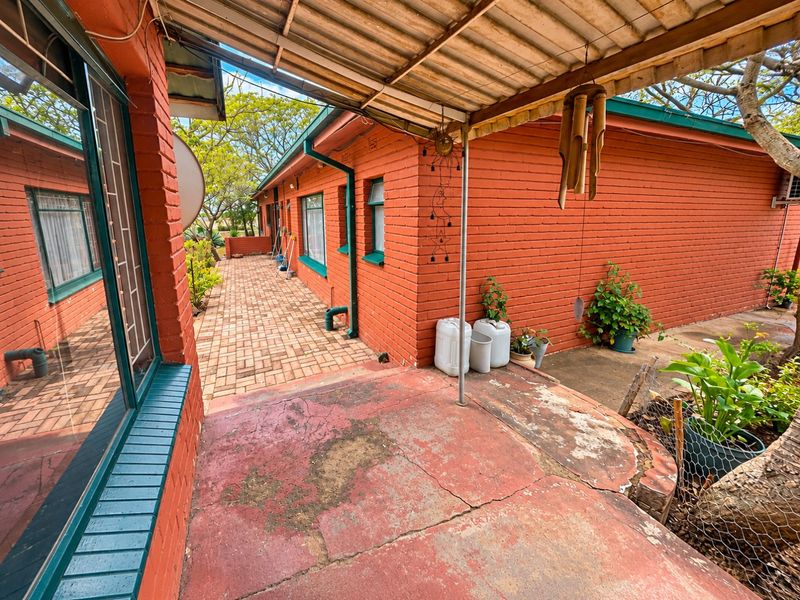 A covered outdoor patio area featuring red brick walls, a paved walkway, and a concrete floor showing signs of wear and cracking.