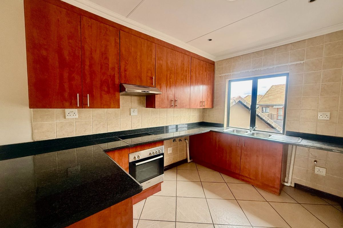 A functional kitchen featuring wooden cabinetry, granite countertops, a built-in oven with hob, and a double sink with tiled backsplash.