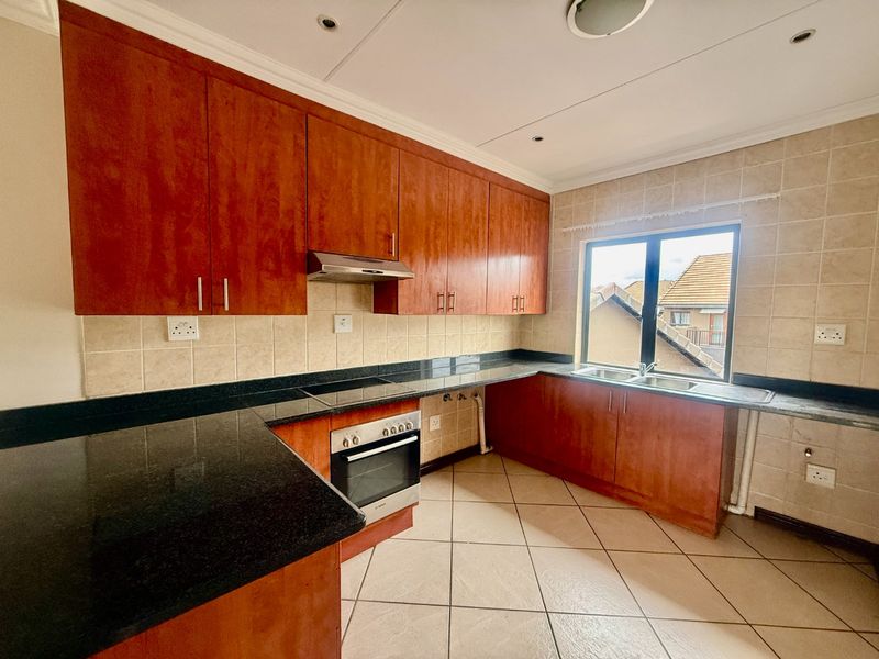 A functional kitchen featuring wooden cabinetry, granite countertops, a built-in oven with hob, and a double sink with tiled backsplash.