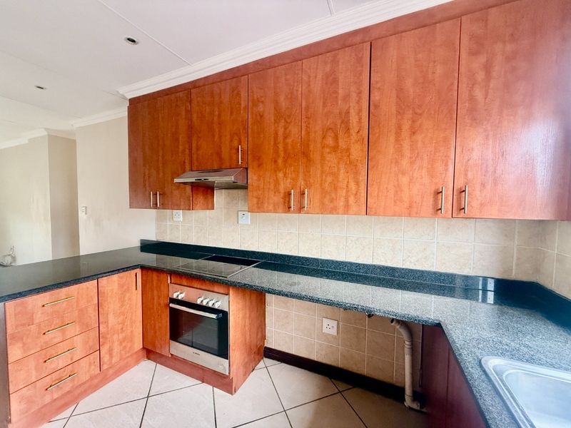 A functional kitchen featuring wood-finish cabinetry, granite countertops, built-in oven, electric hob, and tiled backsplash, offering a clean and practical workspace.