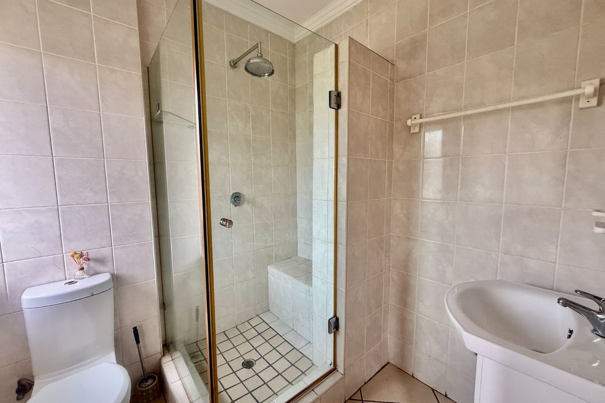 A functional bathroom featuring a glass-enclosed shower with a built-in bench, a pedestal basin, and a standard toilet with neutral wall tiling.