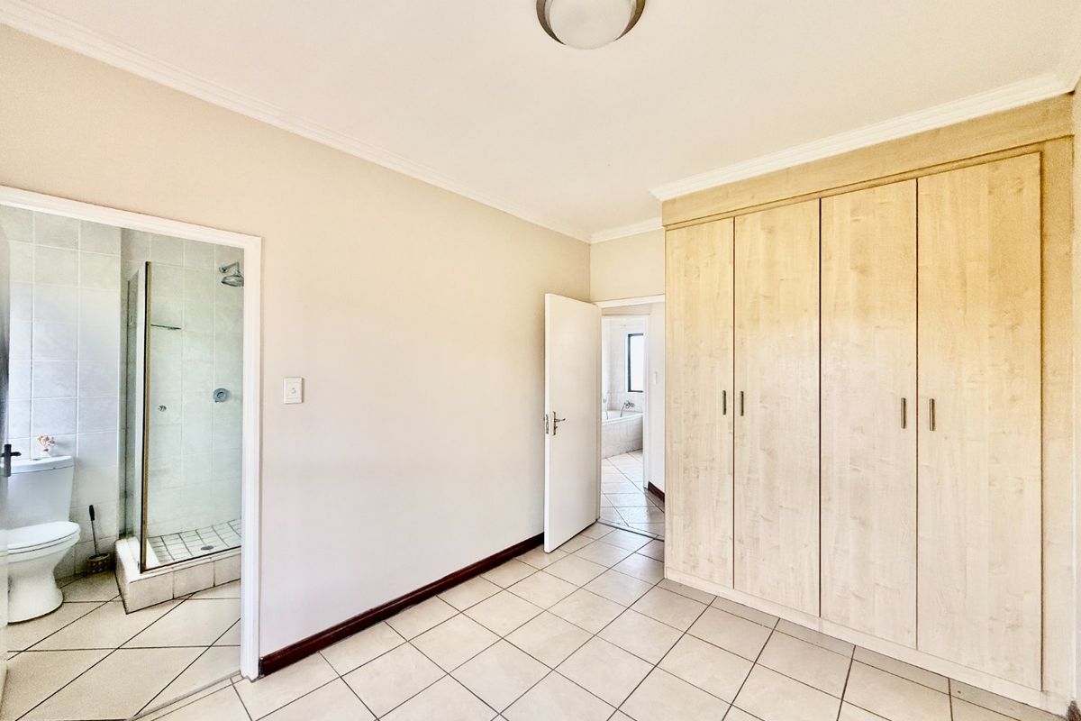 A spacious, empty bedroom featuring light-toned built-in cupboards, tiled flooring, and direct access to an en-suite bathroom.