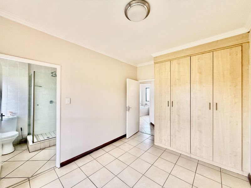 A spacious, empty bedroom featuring light-toned built-in cupboards, tiled flooring, and direct access to an en-suite bathroom.